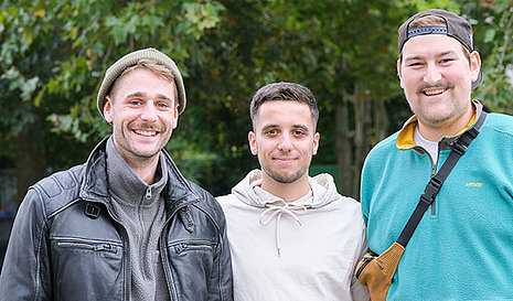 Drei junge erwachsene Männer stehen nebeneinander udn schauen in die Kamera.