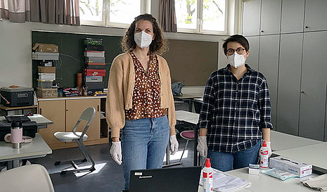 Zwei Frauen mit Mundschutz in einer Corona-Teststation in einem Klassenzimmer.