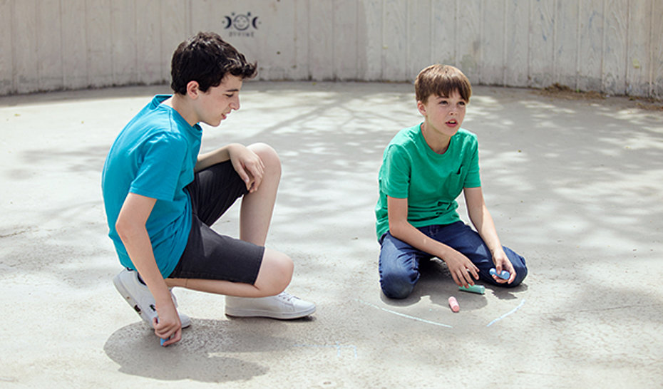 Zwei Jungs mit Straßenmalkreide sitzend auf dem Boden.