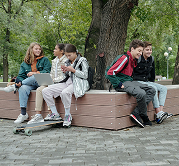 Fünf Schülerinnen und Schüler sitzend auf einer Bank, um einem Baum rum.