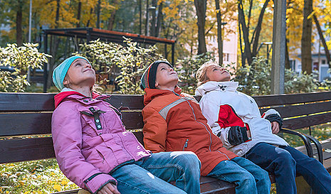 Drei Kinder auf einer Parkbank schauen in den Himmel.