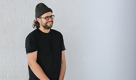 Cooler Typ mit Mütze und Brille vor einer weißen Wand.